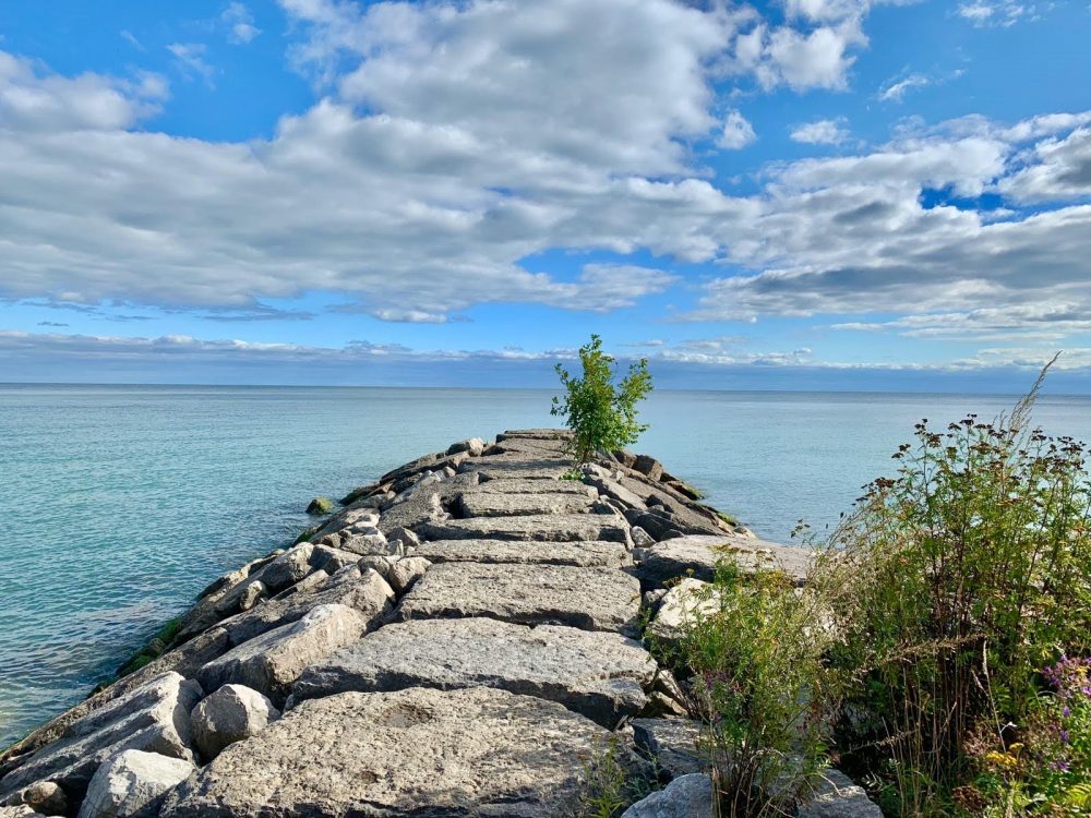 Sunny blue sky with clouds above a rock path leading to an open body of water