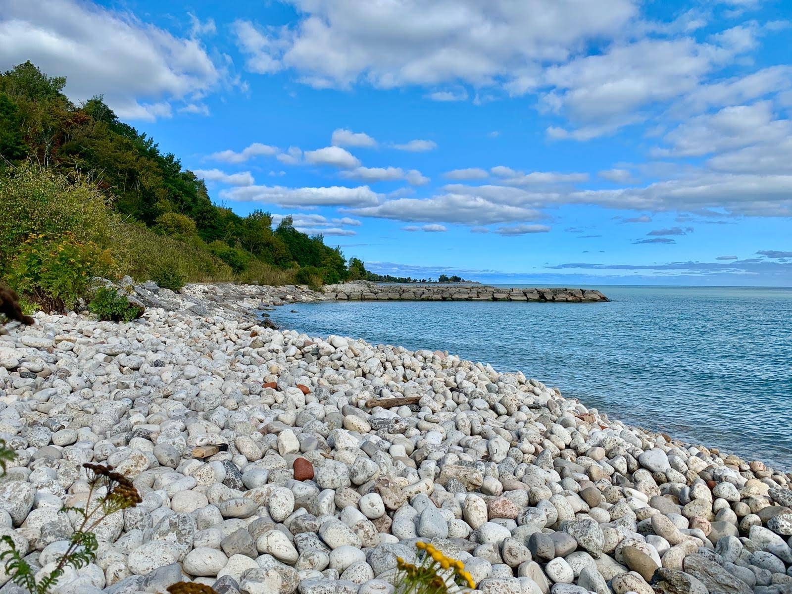 Blue sky with few bright clouds above a rocky shore meeting a lake