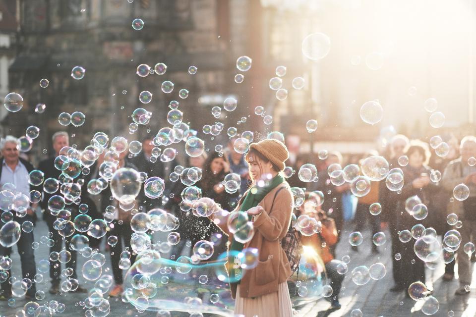 Person with a sweater, scarf, and hat standing in front of a crowd surrounded by bubbles. 