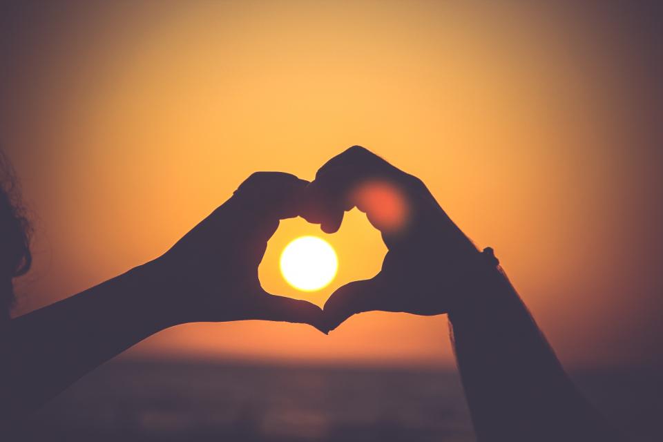 Hands forming a heart in front of a warm sunset. 